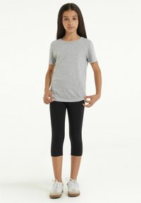 T-shirt gris à manches courtes associé à des leggins capri noirs, complété par des baskets blanches avec des accents beiges. Tissu lisse, design ajusté.