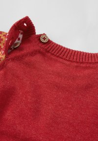 Punainen neulepaita, jossa on ribbireuna, kahdella koristeellisella napilla ja kuvioidulla sisäkauluksella. Suuri tyyli, pehmeä neulemateriaali.