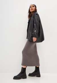 Chaqueta oversized de cuero negro con cremalleras plateadas, combinada con una falda gris de longitud hasta la rodilla y botas negras de tobillo con suelas gruesas.