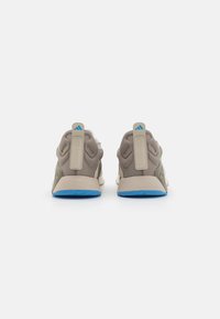 Beige training shoes with textured mesh and synthetic material. Features a blue sole, contrasting back tabs, and subtle branding details.