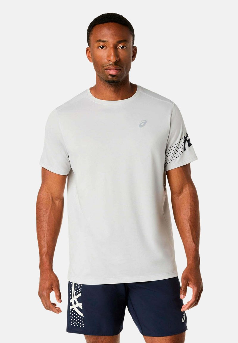 Homme athlétique portant un t-shirt blanc à manches courtes uni et un short bleu marine avec des motifs graphiques blancs, debout face à l'avant.
