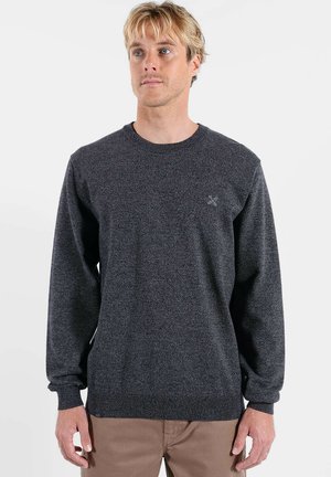 Pull en maille gris foncé avec encolure ronde, manches longues, poignets côtelés et un petit détail logo sur le côté gauche de la poitrine.