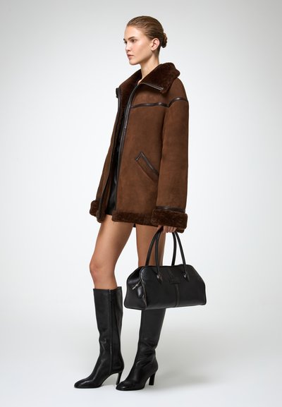 Pruun nubukist sooja jakk mustade nahkakujunditega, kombineeritud põlvekõrguste mustade nahkadega saapade ja sobiva musta käsitaskuga.