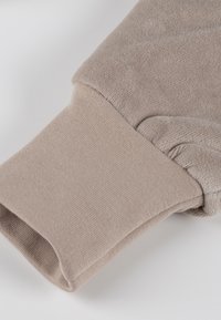 Beige sweatshirt cuff featuring a soft, textured, fleece-like fabric with a ribbed knit finish at the edge for stretch and comfort.