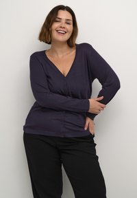 Cardigan albastru marin, cu mâneci lungi, de tip v, cu butoane în față și o textură moale. Asortat cu pantaloni negri pentru un look casual.