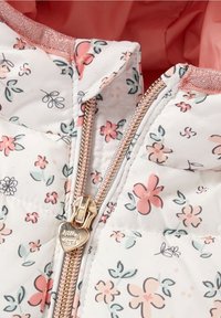 Śnieżnobiała pikowana kurtka w kwiaty z różowymi i zielonymi akcentami. Wyposażona w złoty zamek błyskawiczny z zawieszką w kształcie serca oraz miękką różową podszewkę.