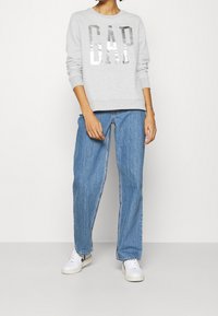 Sudadera gris con letras plateadas "GAP", combinada con jeans de pierna ancha en azul claro y zapatillas blancas con detalles negros.