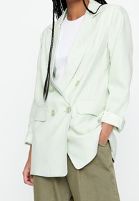 Lysegrøn dobbeltbrystet blazer med en afslappet pasform, der har to forlommer og knapdetaljer. Båret over en hvid top.