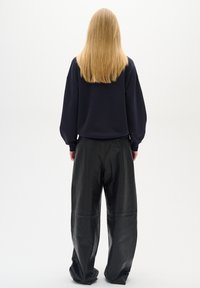 Námořnický sweatshirt s kleslými rameny v kombinaci s širokými kalhotami z černé kůže. Hladký povrch a minimální detaily šití.