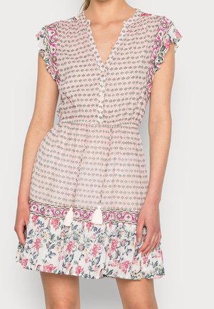 Vrouw met een kort rokje roze jurk met kleine geometrische prints, een bloemenruche zoom, kwastjes in de taille en bloemenrand op de mouwen.
