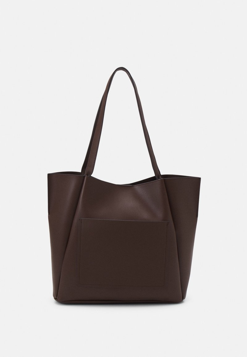 Sac cabas en cuir marron foncé avec de longues poignées et une grande poche avant, présenté sur un fond clair uni.