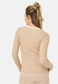 Langärmliges, geripptes Strickoberteil in Beige mit weitem Ausschnitt und taillierter Silhouette, das eine subtile Textur und einen sauberen, gesäumten Saum aufweist.