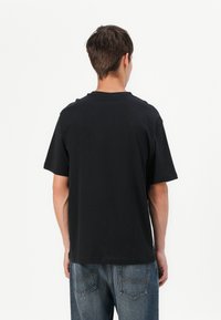 Black cotton t-shirt with a crew neck and short sleeves, featuring a relaxed fit. Textured fabric with no visible patterns or graphics.