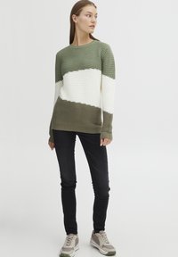 Pull en tricot vert et blanc rayé avec une texture côtelée, col rond et manches longues, associé à un jean skinny noir et des baskets.