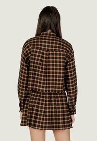 Abito camicia a quadri neri e marroni con maniche lunghe, gonna svasata e chiusura con bottoni sul retro, caratterizzato da una trama in tessuto leggero.