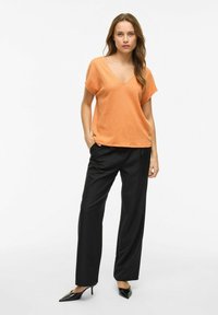 Pomarańczowa bluzka z krótkim rękawem i dekoltem w szpic, o strukturze fakturowej, zestawiona z czarnymi spodniami typu wide-leg i czarnymi szpilkami.