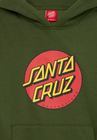 Felicidade olive verde com capuz apresenta um grande gráfico de círculo vermelho com "SANTA CRUZ" em letras amarelas e pretas. Inclui bolso frontal.