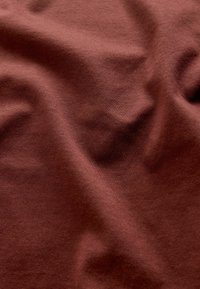 Brązowa tkanina o gładkiej fakturze, z delikatnymi zagnieceniami i fałdami, wskazująca na lekki i elastyczny materiał.