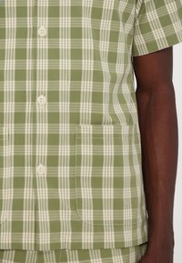 Πλαίσιο κοντομάνικο πουκάμισο πράσινης και κρεμ λεπτομέρειας, σε relaxed fit, με δύο μπροστινές τσέπες και κλείσιμο με κουμπιά. Υφαντό βαμβακερό ύφασμα.
