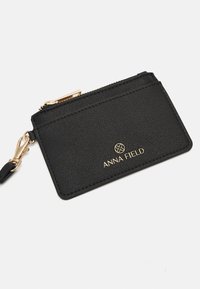 Porte-cartes en cuir noir avec fermeture éclair et fermoir dorés, avec le nom de la marque ANNA FIELD en lettres dorées sur le devant.