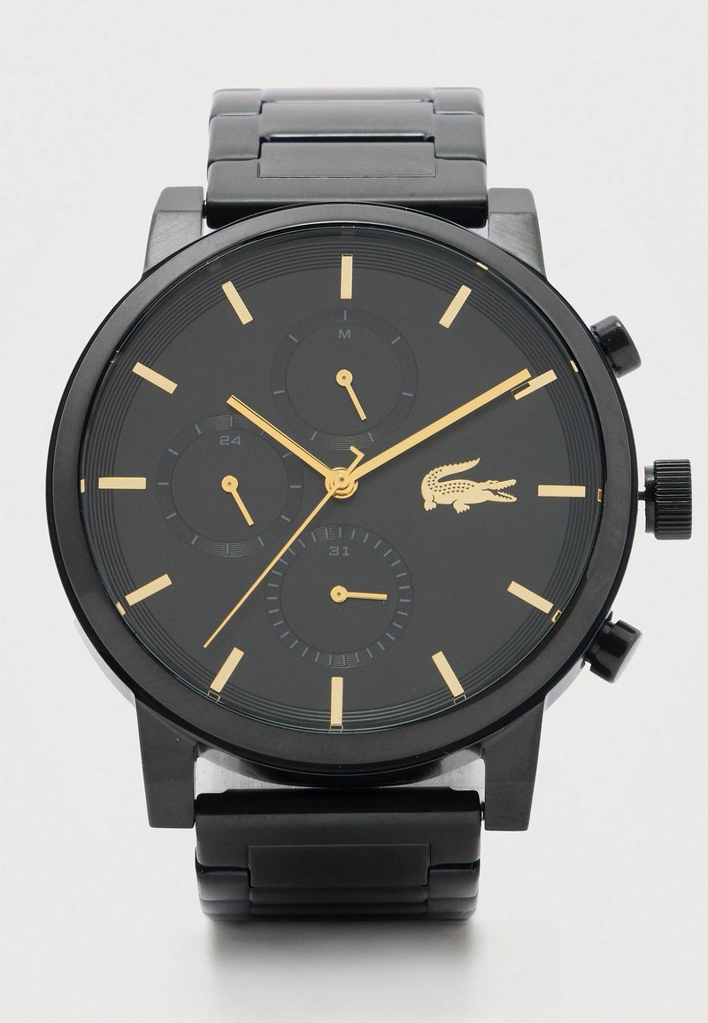 Zwart metalen horloge met gouden uurmarkeringen, drie subdialen en een gouden krokodillogo aan de rechterkant van de wijzerplaat.