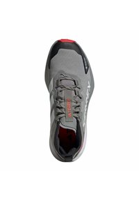 Chaussure de sport grise avec une tige texturée, des accents rouges et des détails noirs. Elle dispose d'un design à lacets et d'un logo sur le côté.
