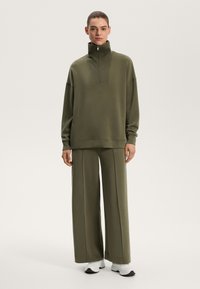 Olivgrön sweatshirt med hög krage och halvdragkedja, matchad med vida byxor i samma färg, allt i ett slätt, texturerat tyg.