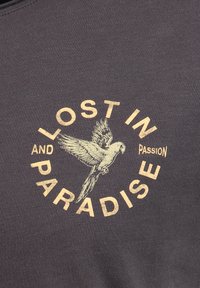Illustration eines fliegenden Papageis mit geschwungenem Text "LOST IN PARADISE" und kleinem Text "AND PASSION" auf dunklem Stoffhintergrund.