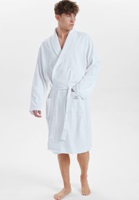 Bata de baño de punto de waffles blanca con cuello de chal, mangas largas, cinturón de lazo y dos bolsillos frontales. Textura suave, diseño a la altura de la rodilla.