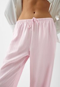 Lightweight, pink pajama pants with vertical white stripes, elastic waistband, and drawstring detail. Soft texture, relaxed fit.