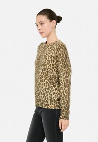 Maglione leopardato in toni beige e marroni, realizzato in un tessuto morbido, con scollo rotondo e maniche lunghe, abbinato a jeans neri.