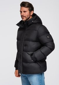 Czarna kurtka puchowa z kapturem, z dużymi pikowanymi sekcjami, guzikami z przodu i naszywką logo na rękawie. Slim fit.