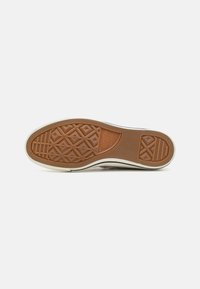 Rubber shoe sole with a textured surface, featuring a brown color with geometric patterns and white accent around the edge.