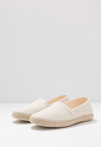 Beige kengät ilman nyörejä, valmistettu Strukturoidusta kankaasta, jossa on joustavat sivupaneelit ja kudottu juuttipohja. Sileä sisävuori. Pyöreä kärkipohjamalli.