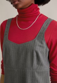 Grau gestreiftes Kleid mit quadratischem Ausschnitt über einem enganliegenden roten Rollkragenpullover. Eine silberne Kettenhalskette fügt Details hinzu. Strukturierter Stoff ist sichtbar.