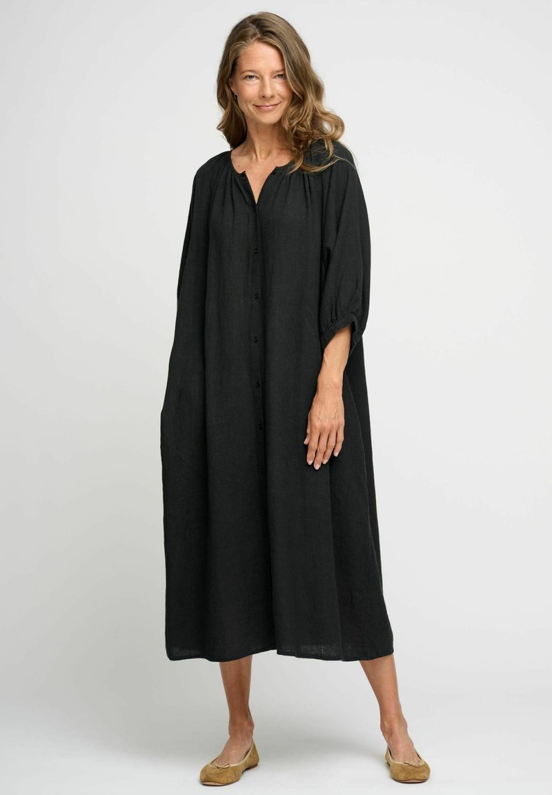 Rochie din in negru, cu o croială lejeră, cu închidere pe butoane în față și mâneci 3/4. Prezintă un guler rotund și buzunare laterale, ajungând până la jumătatea gambei.
