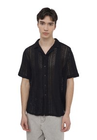 Camicia nera a maniche corte realizzata in un materiale a maglia aperta e testurizzata, con chiusura a bottoni frontale, caratterizzata da strisce verticali e colletto standard.