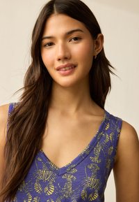 Top viola senza maniche con scollo a V, caratterizzato da un motivo astratto giallo. Il tessuto ha una texture liscia e il design include motivi ad anello.