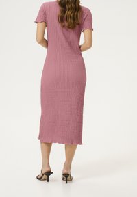 Waffle-texturiertes, knielanges Kleid in staubigem Rosa mit kurzen Ärmeln, seitlichen Schlitzen und einer weichen, entspannten Silhouette. Schwarze High-Heelsandalen.