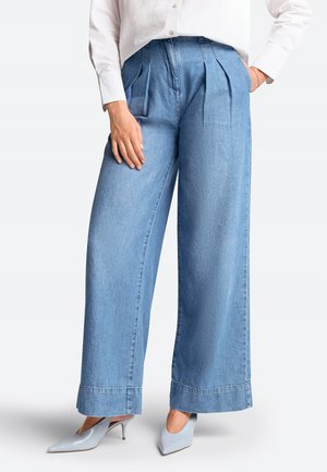Pantalons en denim bleu clair à jambes larges avec des plis à la taille et un ourlet brut. Associés à des talons aiguilles bleu clair.
