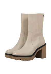 Botas de tobillo beige hechas de cuero texturizado, con un tacón marrón grueso y suela estriada, con un diseño sin costuras y sin herrajes visibles.