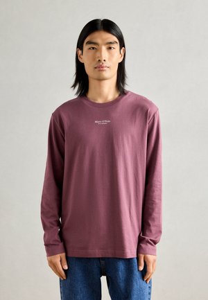 Langermet, maroon bomull T-skjorte med rund hals og hvitt logo sentrert på brystet, paret med løse blå denimjeans.
