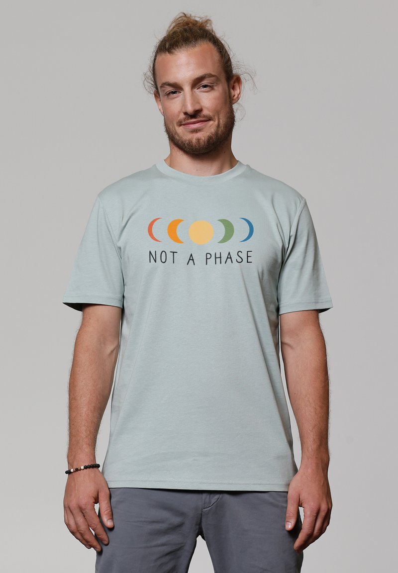 T-shirt en coton bleu clair avec un graphique des phases lunaires colorées et le texte "CE N'EST PAS UNE PHASE" en noir, col rond, manches courtes.