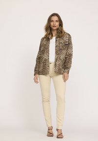 Veste à imprimé léopard avec deux poches avant, associée à un jean skinny crème et des sandales à lanières. Texture de tissu lisse, coupe décontractée.