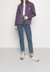 Lila jacka med tryckknappar, framfickor, i kombination med ljusblå tapered jeans och vita sneakers med gula detaljer.