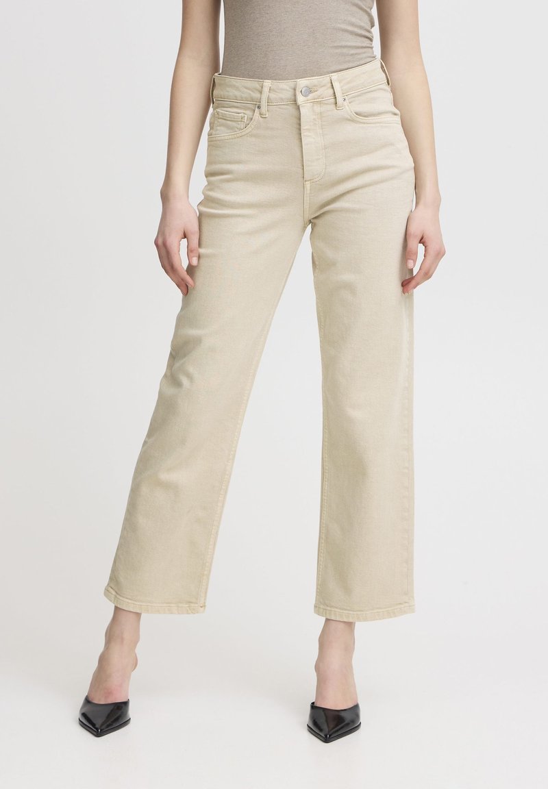 Jeans beige a vita alta con design a gamba dritta, realizzati in denim; presentano tasche frontali e dettagli in metallo argentato, abbinati a tacchi neri a punta.