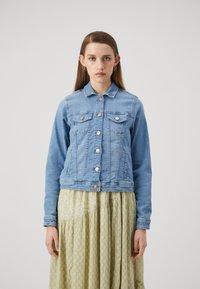 Chaqueta de mezclilla azul claro con cuello, cierre de botones y dos bolsillos en el pecho. Presenta botones en tono cobre y una cintura entallada. Mangas largas.
