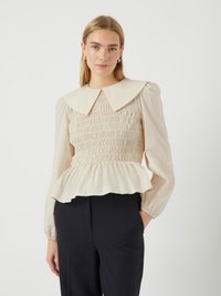 Cremefarbene Bluse mit großem Kragen, gesmoktem Oberteil und gerafftem Peplum-Saum. Lange Ärmel mit elastischen Bündchen. Tragen Sie sie mit schwarzen Hosen.