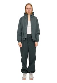 Dark green windbreaker jacket with a hood, paired with matching loose-fit pants. Both feature a smooth texture and elastic cuffs.