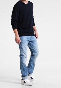 Pull en maille bleu marine à col en V, tissu léger, associé à un jean bleu clair. Baskets blanches avec des accents bleu marine. Silhouette décontractée et ajustée.